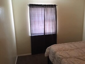 Una habitación con una cama, una ventana con cortinas traslúcidas y una pared lisa.