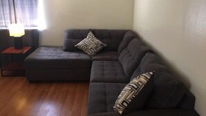 Ein Wohnzimmer mit einem dunkelgrauen Sofa, einem kleinen Hocker und einer Lampe auf einem Beistelltisch.