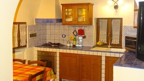 A kitchen with an archway, wooden cabinets, a tiled backsplash, a stove, and a dining table with chairs. - Two-room apartment barn in farmhouse with swimming pool (Scandicci)