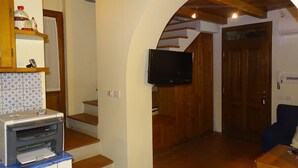 A living room with a fireplace, a flat-screen TV, and a staircase leading to another room. - Two-room apartment barn in farmhouse with swimming pool (Scandicci)