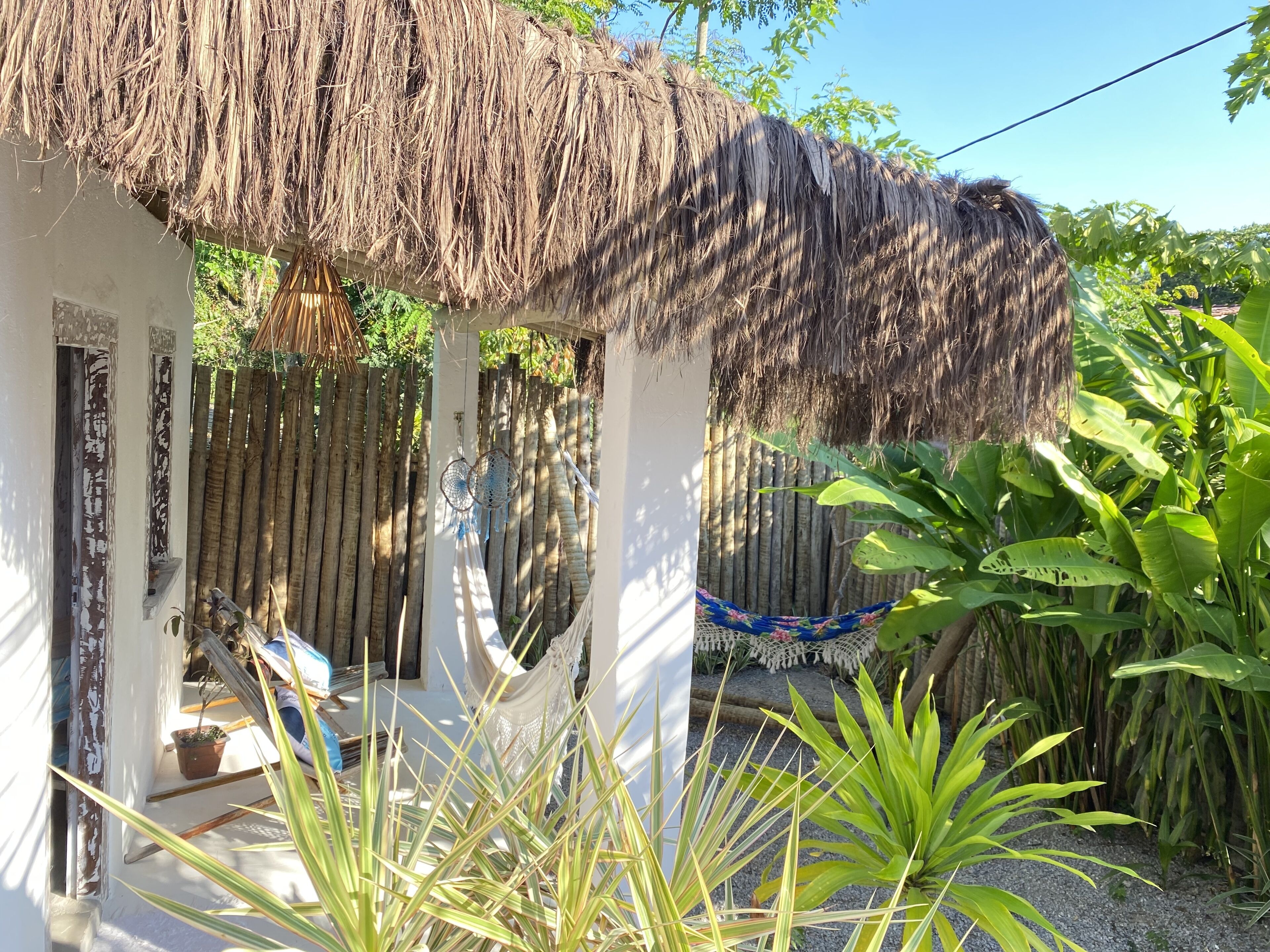A thatched-roof structure with a hammock and a small garden area with plants.