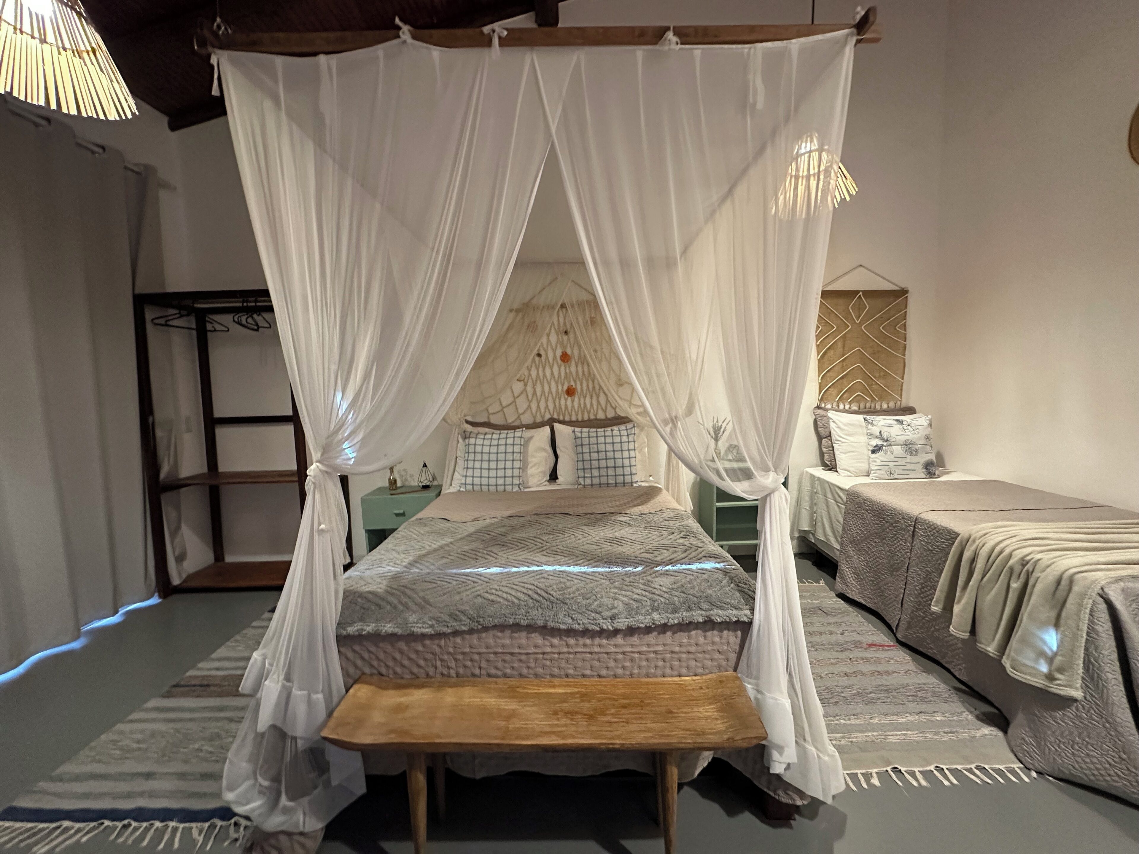 A bedroom with a canopy bed, a wooden bench, and a nightstand.