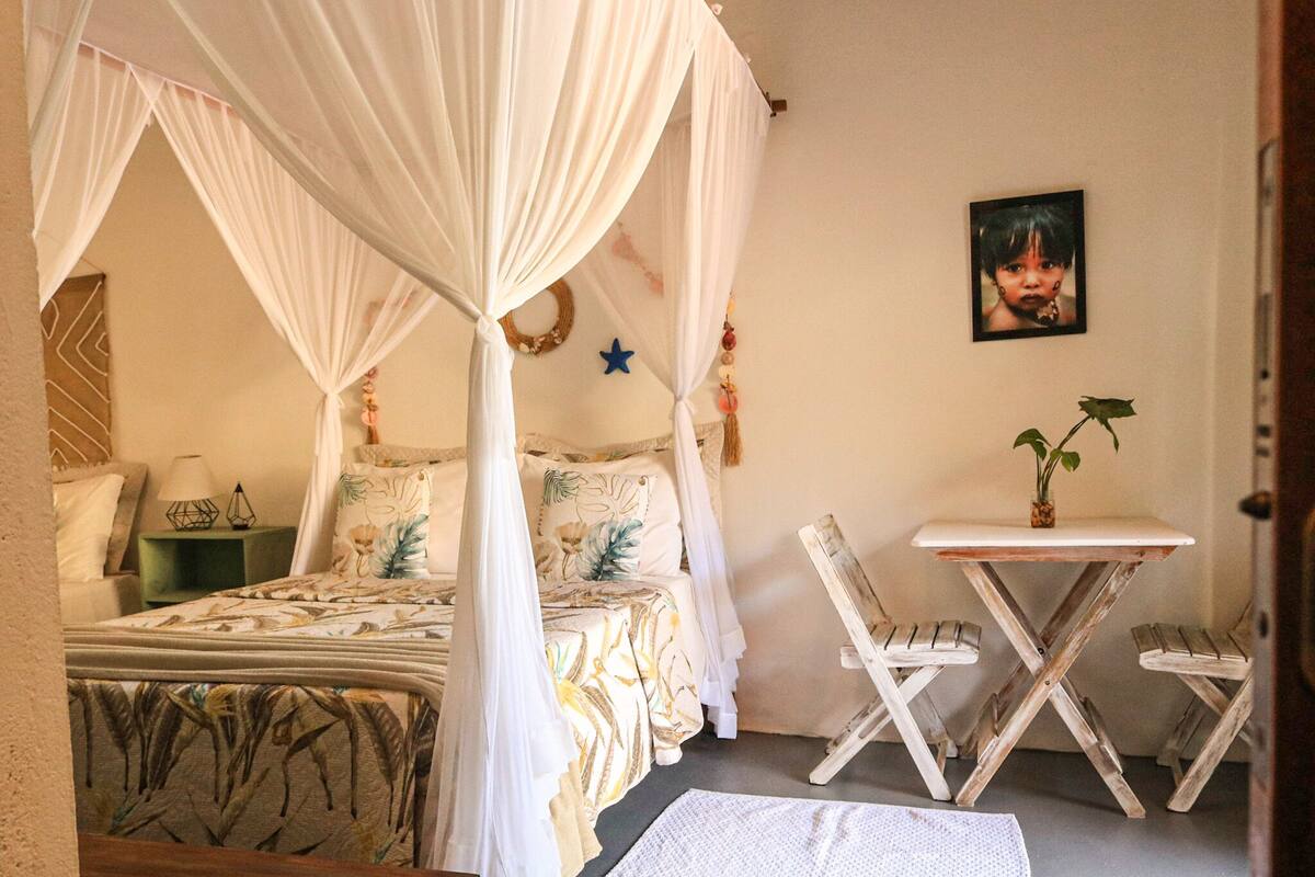 A bedroom with a canopy bed, a small table with chairs, a wall-mounted picture, and a decorative star.