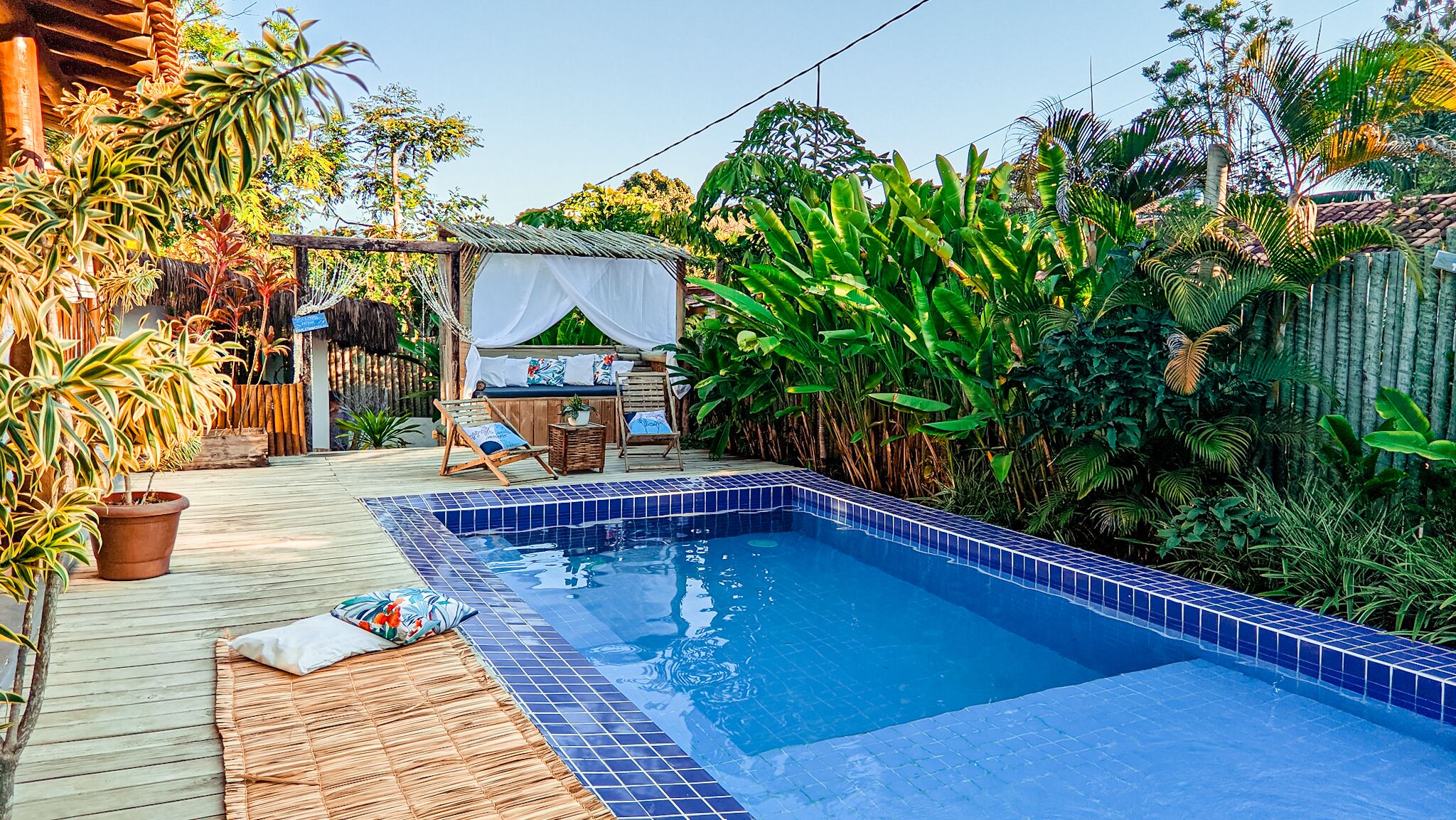 A swimming pool with blue tiles, surrounded by lush greenery and a wooden deck.