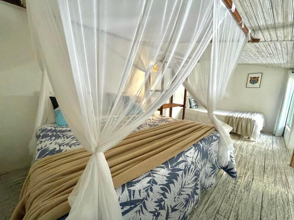 A room with a bed covered by a canopy, a wooden floor, and a chair in the background.