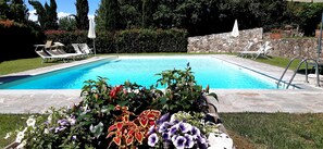 Ein rechteckiger Pool mit einer Steinmauer und einer Rasenfläche mit Blumen und Liegestühlen.