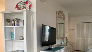 A hotel room with a white wardrobe, a television, a mirror, and a bed with a blue and white bedspread. - Beachside Unit 36 - Key Colony (Key Colony Beach)
