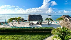 A beachside resort with a pool area, thatched-roof structures, and palm trees. - Beachside Unit 36 - Key Colony (Key Colony Beach)