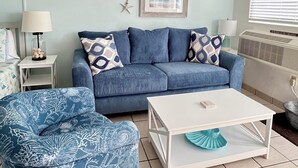 A living room with a blue sofa, patterned armchair, white coffee table, and a framed picture on the wall. - Beachside Unit 36 - Key Colony (Key Colony Beach)
