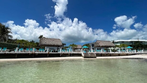 A beachside resort with thatched-roof structures, clear turquoise water, and a white sandy beach. - Beachside Unit 14 - Key Colony (Key Colony Beach)