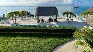 A beach resort with a thatched-roof hut, lounge chairs, and a clear view of the ocean. - Beachside Unit 14 - Key Colony (Key Colony Beach)