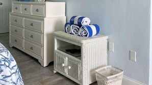 A bedroom with a dresser, a television mounted on the wall, a wicker storage unit, and a basket on the floor.