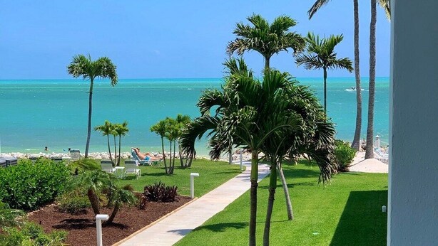 A well-maintained lawn with palm trees, a pathway, and a view of the ocean. - Beachside Unit 34 - Key Colony (Key Colony Beach)