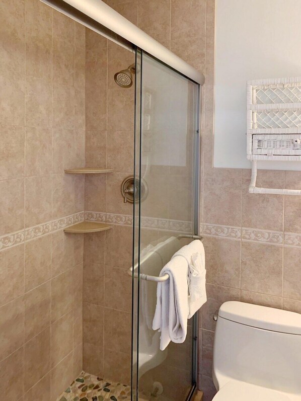 A glass-enclosed shower with a handheld showerhead, a towel rack with a towel, and a toilet. - Beachside Unit 34 - Key Colony (Key Colony Beach)