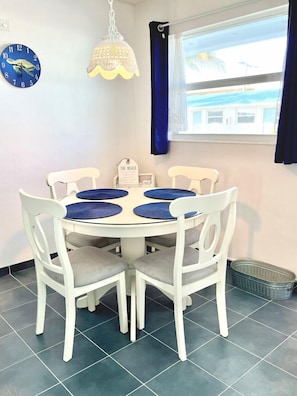 Een eetruimte met een ronde tafel, witte stoelen en een decoratieve klok aan de muur.