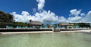 A beachside resort with thatched-roof structures, clear turquoise water, and a white sandy beach. - Beachside Unit 33 - Key Colony (Key Colony Beach)