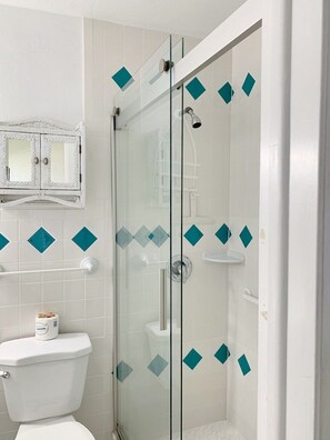 A bathroom with a glass-enclosed shower, white tiles, and a toilet. - Beachside Unit 33 - Key Colony (Key Colony Beach)