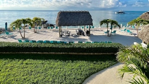 Un resort frente a la playa con estructuras de techo de paja, sillas de descanso y vista al mar.