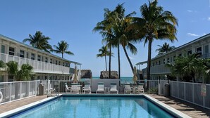 A pool area with lounge chairs and palm trees, surrounded by buildings with balconies. - Beachside Unit 29 - Key Colony (Key Colony Beach)
