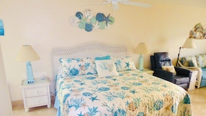 A bedroom with a bed, two nightstands, a chair, and a ceiling fan. - Beachside Unit 26 - Key Colony (Key Colony Beach)