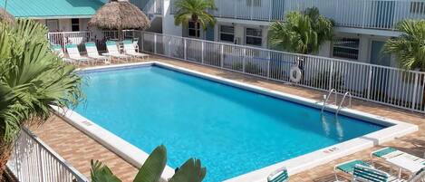 A pool area with lounge chairs and a thatched-roof structure.