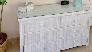 A room with a white wicker console table, a mirror with a lattice frame, a potted plant, a lamp, and a digital clock. - Beachside Unit 26 - Key Colony (Key Colony Beach)