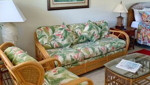 Ein Wohnzimmer mit einer Couch, zwei Korbstühlen, einem Glastisch und einer Lampe.