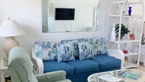 A living room with a blue sofa, a green armchair, a white coffee table, and a white shelving unit with decorative items. - Beachside Unit 27 - Key Colony, Beachside Unit 27 - The Beach is Calling You! (Key Colony Beach)