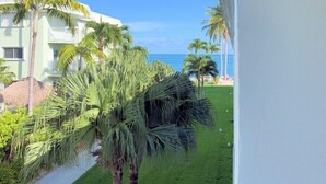 Vista de un balcón de hotel con cielo azul despejado, palmeras y un área ajardinada.