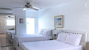 Habitación de hotel con dos camas, un ventilador de techo, un cuadro y vista a la playa.