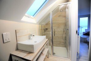 A modern bathroom with a skylight, a glass shower enclosure, and a wooden vanity. - Gull Rock is a Frontline House above Porthmeor Beach, with Amazing Sea Views (St Ives)