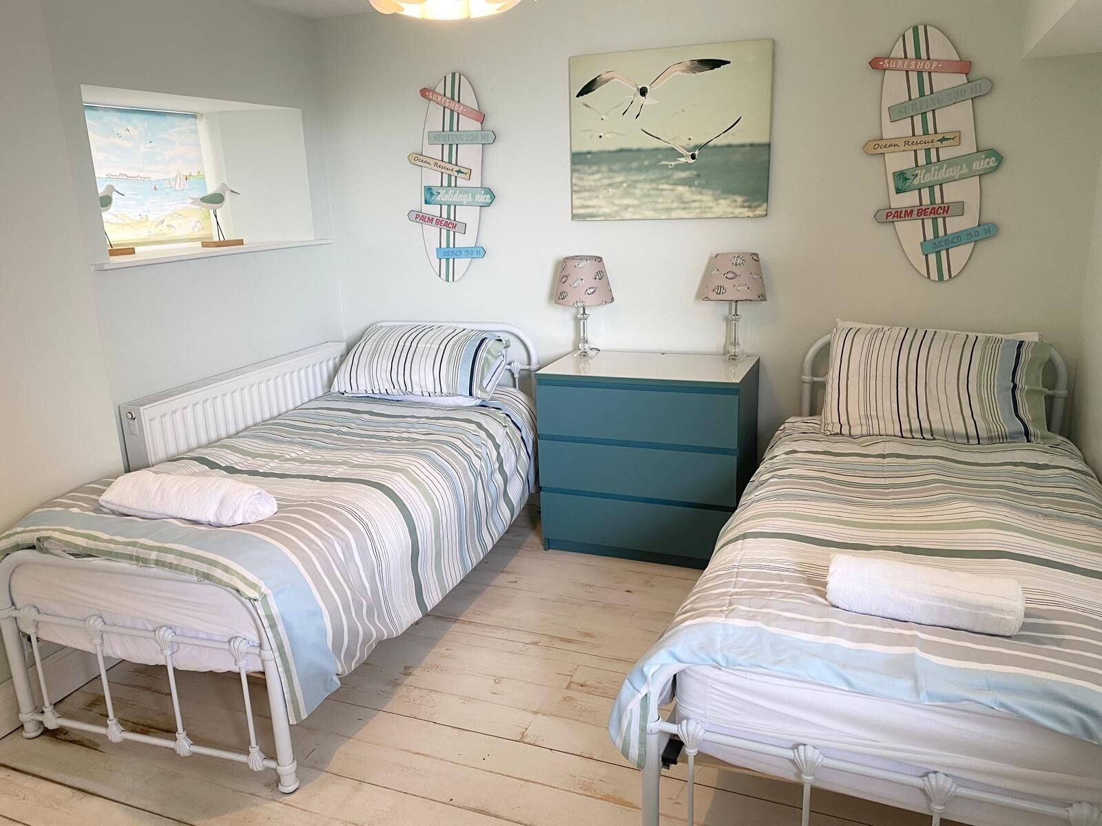 Une chambre avec deux lits, une commode et une fenêtre donnant sur la mer.