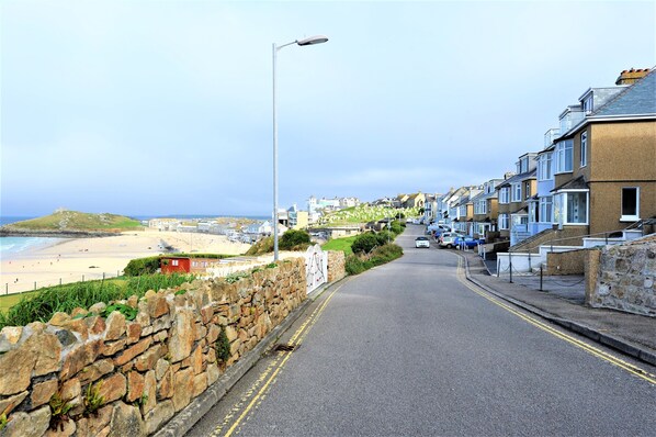 A coastal street with stone walls, a beach, and residential buildings. - Gull Rock is a Frontline House above Porthmeor Beach, with Amazing Sea Views (St Ives)