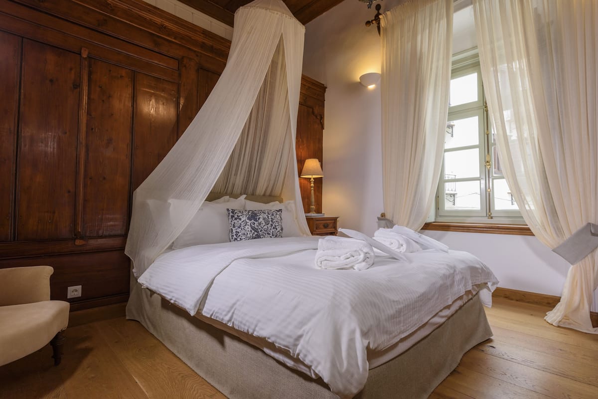 A bedroom with a four-poster bed, a bedside table with a lamp, and a window with curtains.