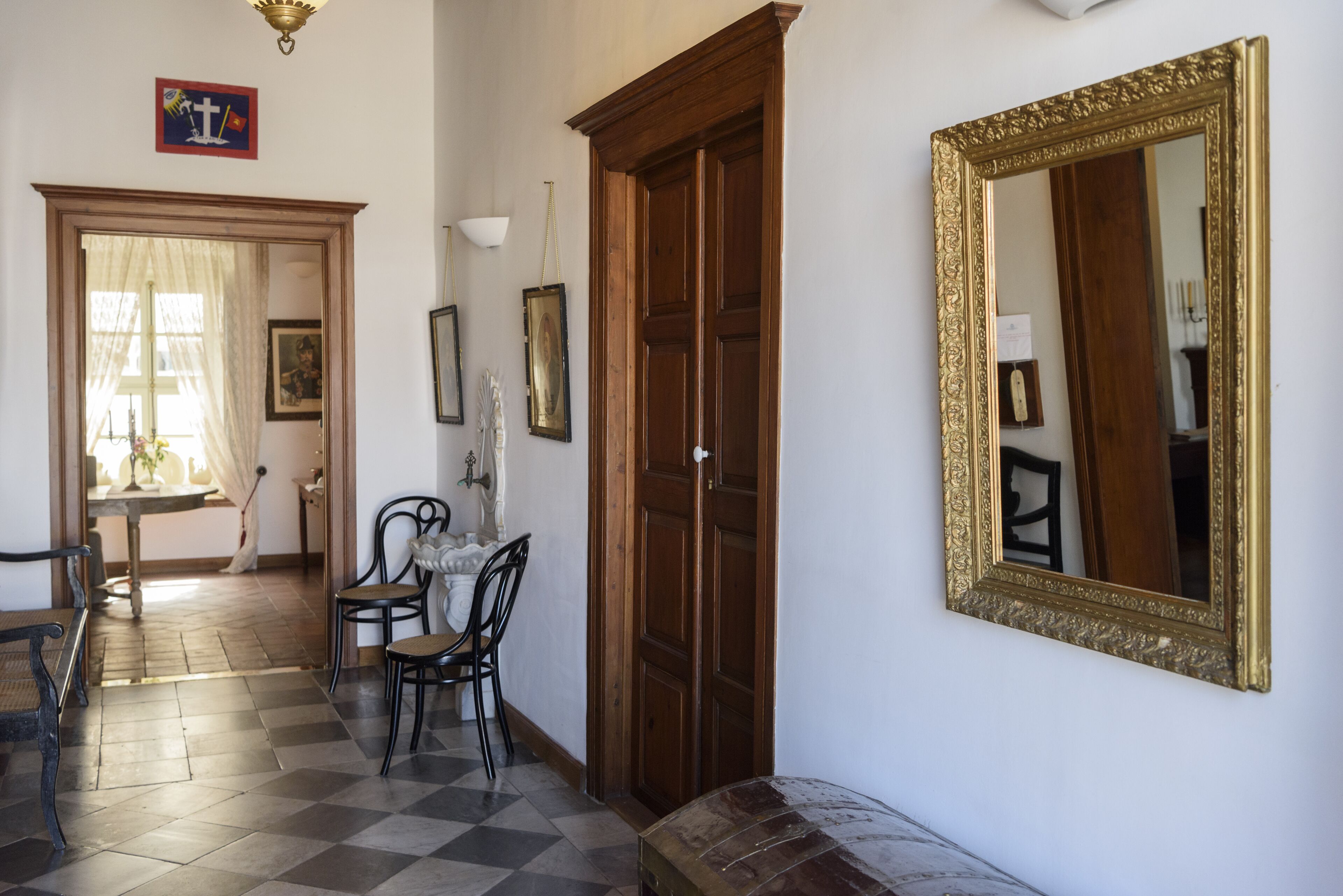 A room with a checkered floor, wooden door, and a large ornate mirror.