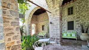 A stone courtyard with a green sofa, white metal chairs, and a table. - Cotommatae Hydra 1810 (Hydra)