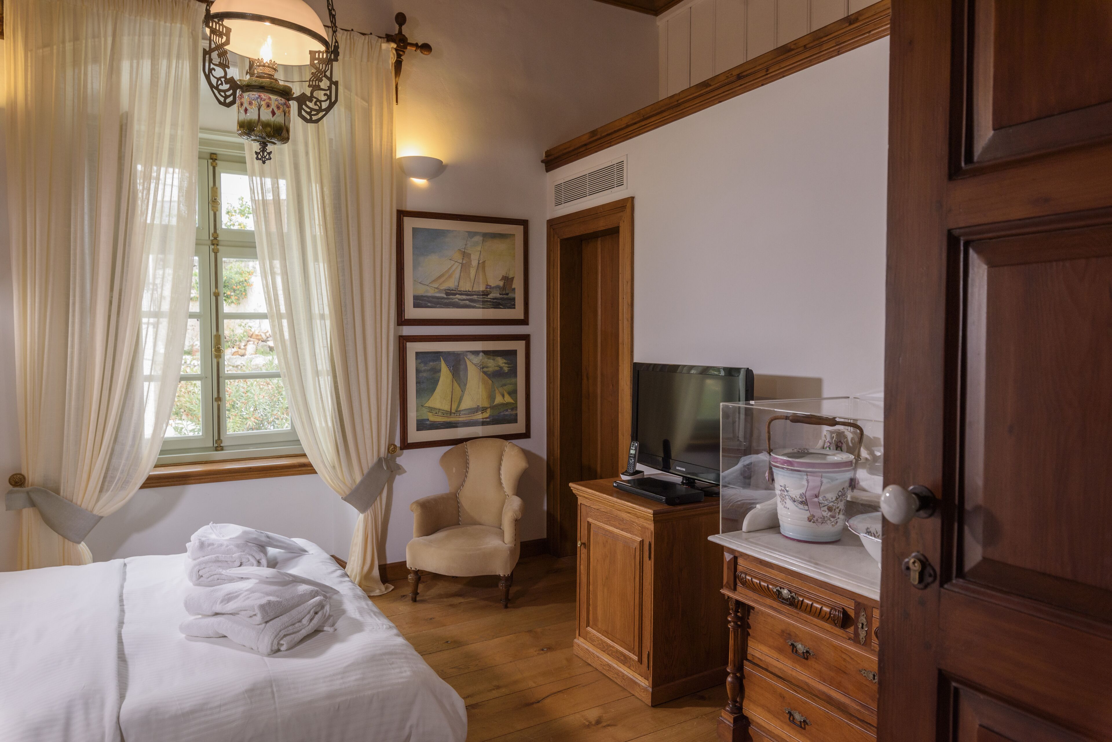 A hotel room with a bed, a chair, a desk with a television, and a window with curtains.