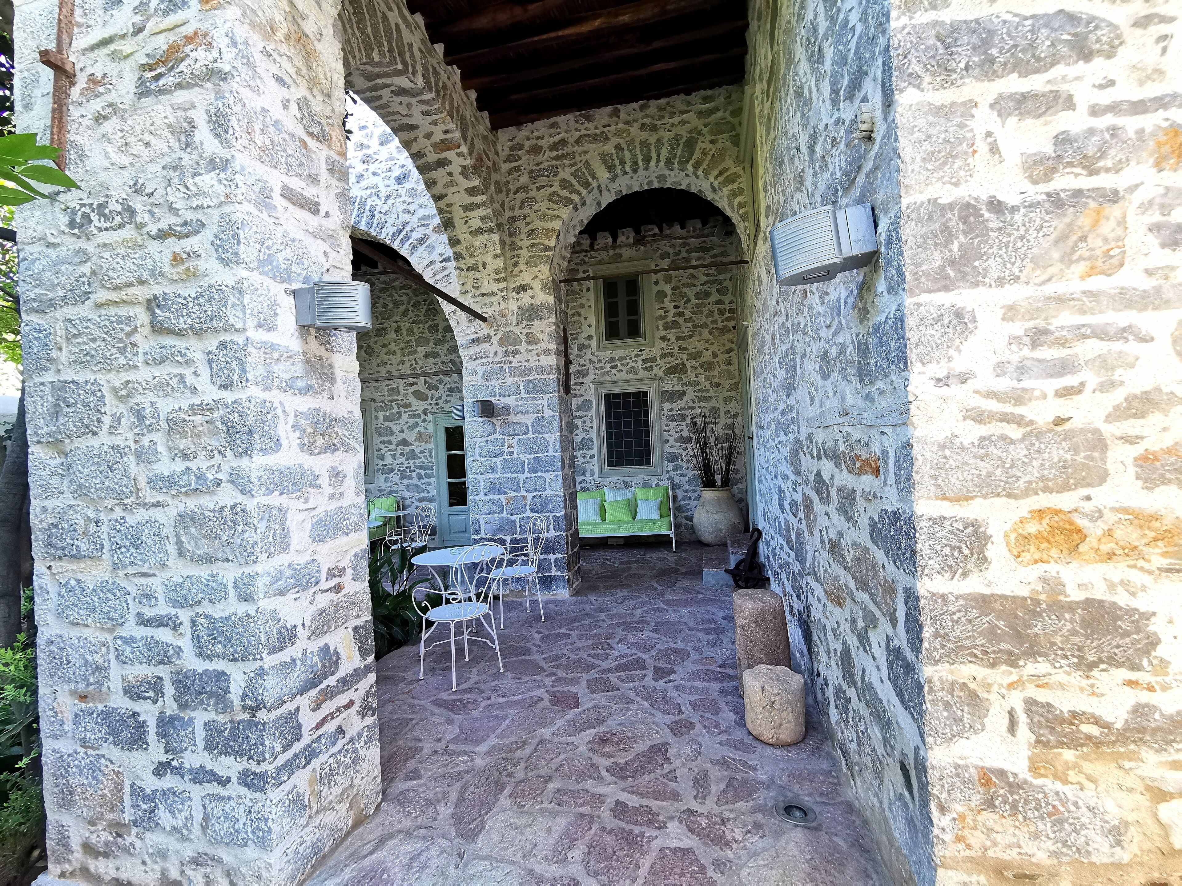 A stone courtyard with a bench, chairs, and a potted plant.