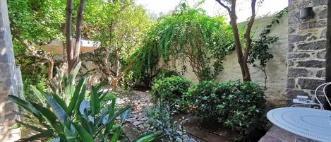 A garden with stone walls, a metal table, and various plants.