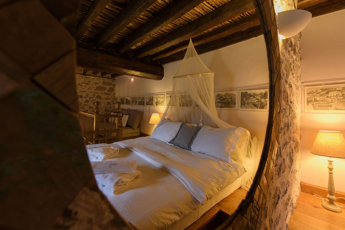 A bedroom with a bed, a nightstand, a lamp, and a stone wall.