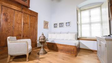 Una habitación con un armario de madera, un sillón blanco, un banco de madera y una ventana con persianas.