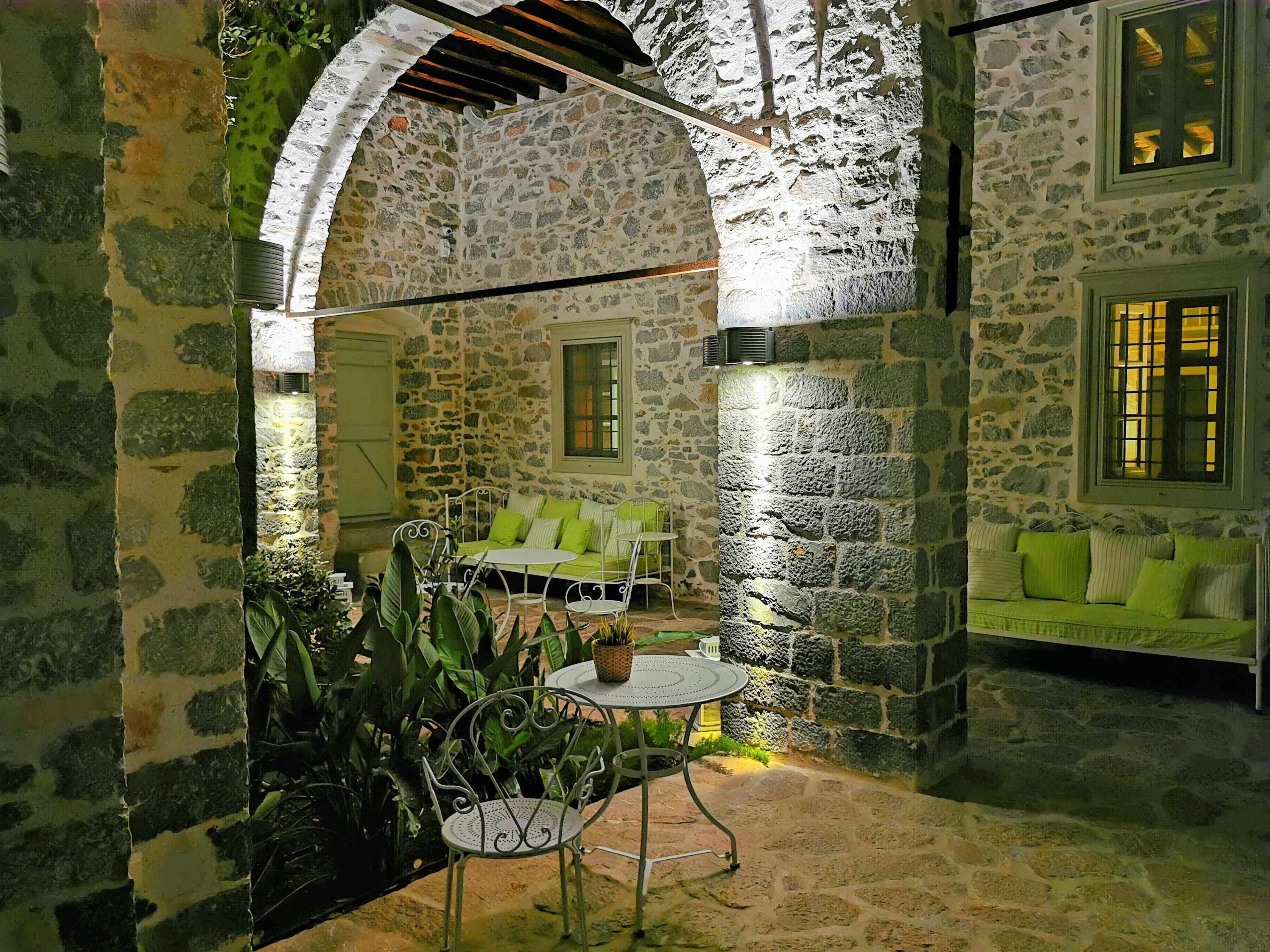 Un patio con paredes de piedra, un sofá verde, una mesa redonda y sillas de metal.
