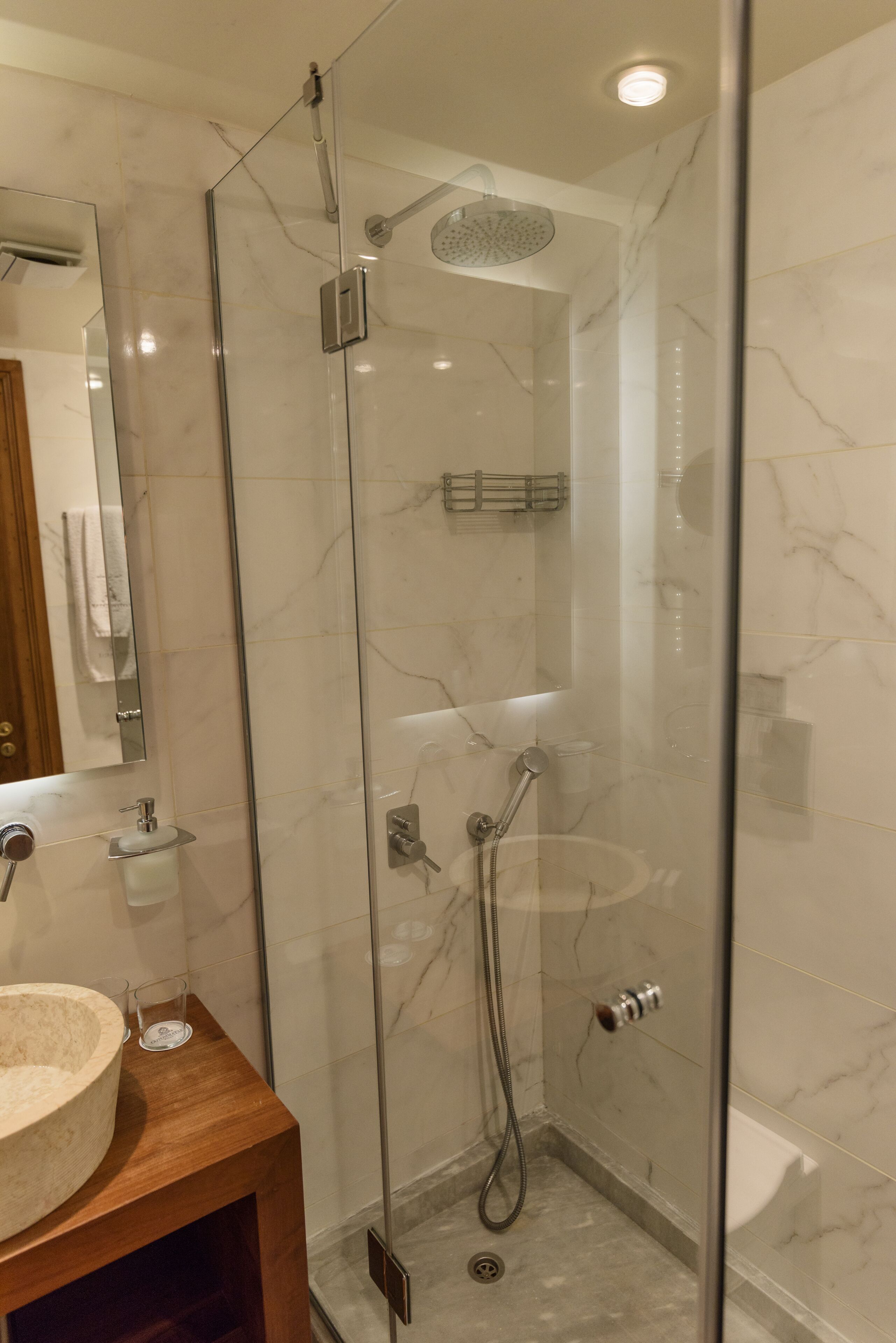 A modern bathroom with a glass-enclosed shower, a wooden vanity with a sink, and marble-tiled walls.