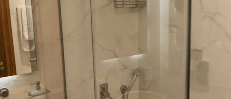 A modern bathroom with a glass-enclosed shower, a wooden vanity with a sink, and marble-tiled walls.