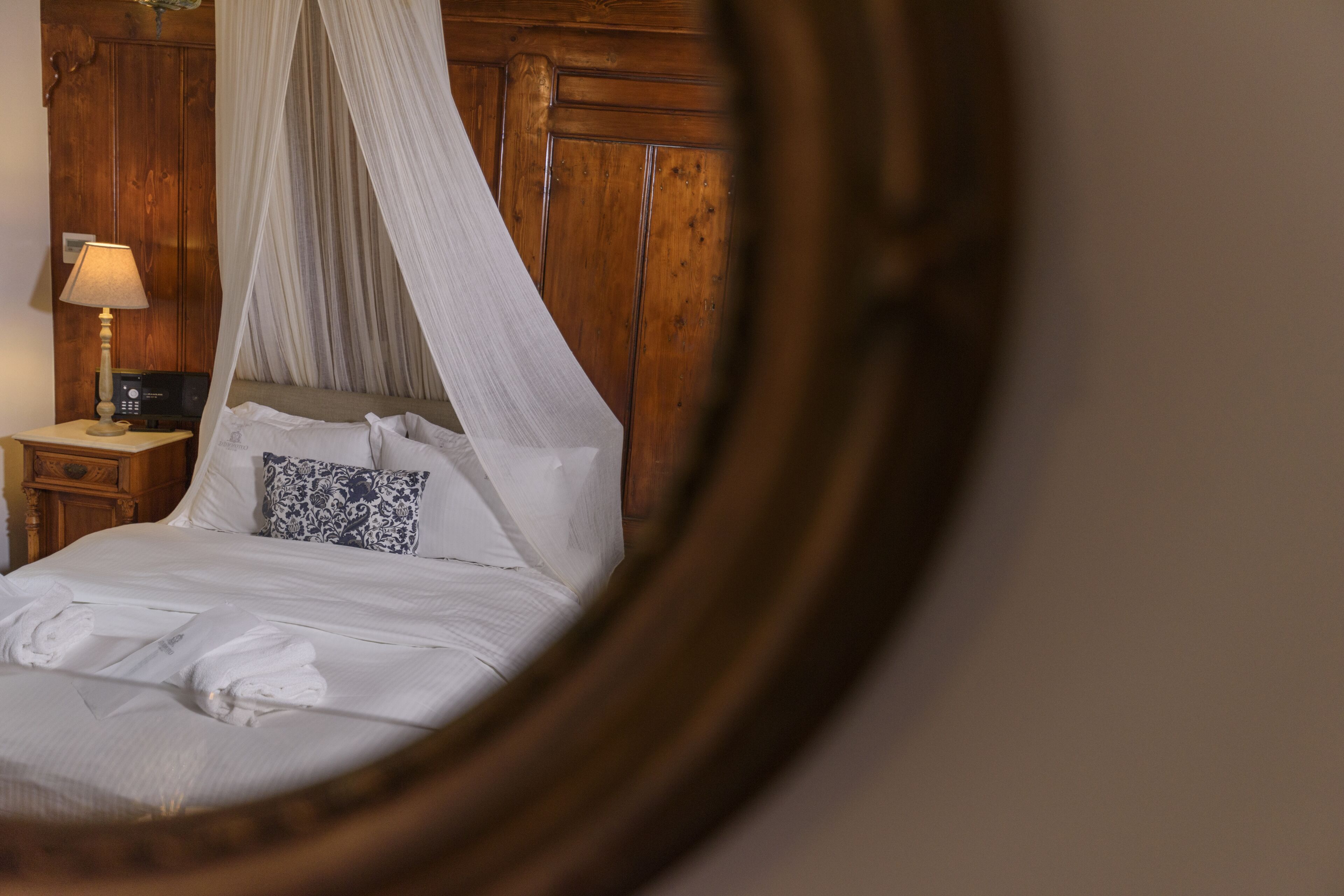 A bedroom with a canopy bed, wooden headboard, bedside table with a lamp, and a nightstand.