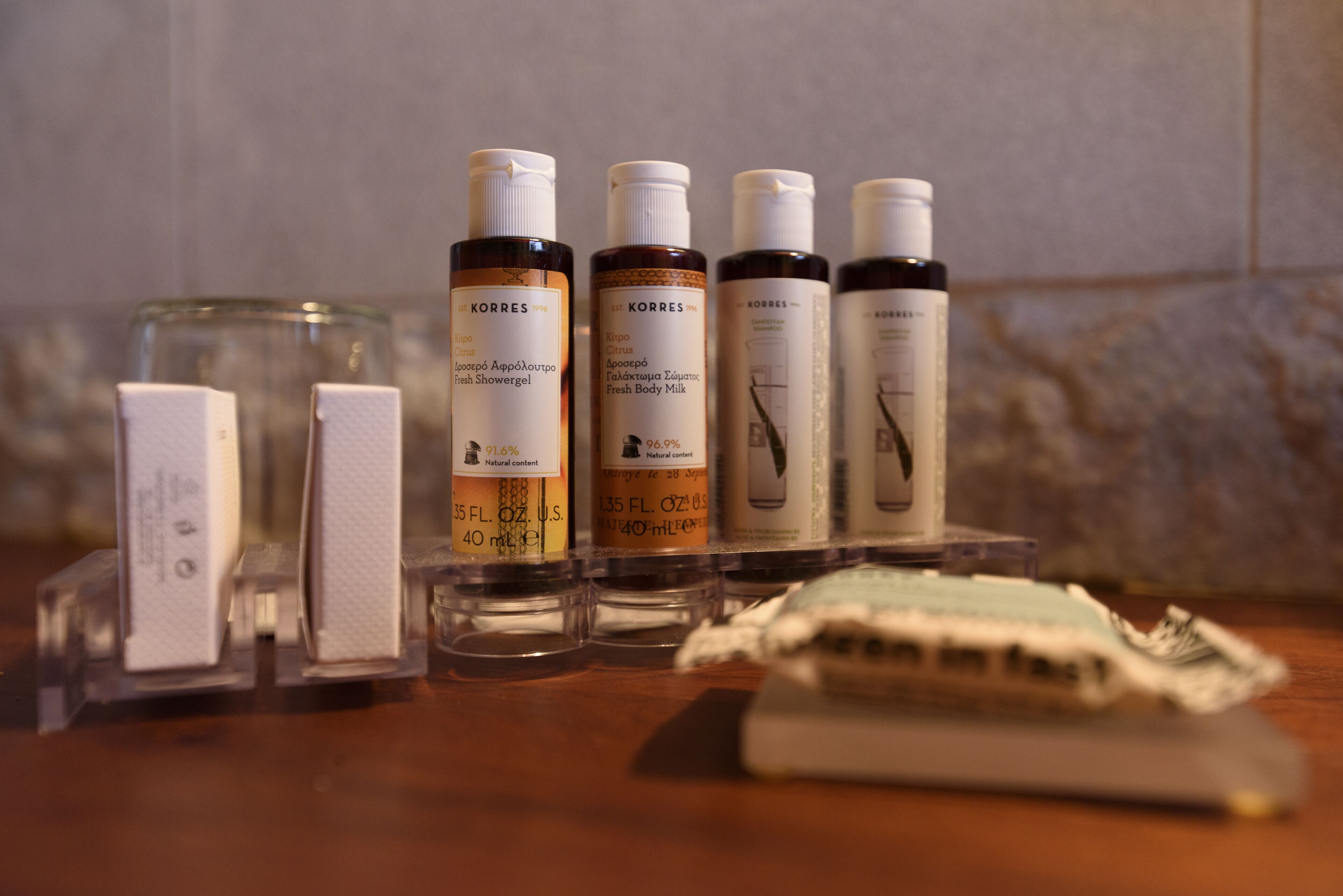 A set of toiletries including Korres shower gel, Korres body milk, and Korres body lotion on a wooden surface.