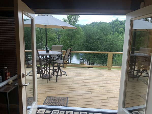 An open deck with a table and chairs, a welcome mat, and a view of a lake surrounded by trees. - Welcome to our lake house in this "tranquil cove" on Lake Chatuge (Hiawassee)
