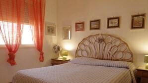 Een slaapkamer met een bed, gordijnen, een nachtkastje met een lamp en ingelijste foto’s aan de muur.