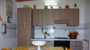 Een keuken met houten kastjes, een gasfornuis, een spoelbak en een tafel met een tafelkleed met een fruitprint.