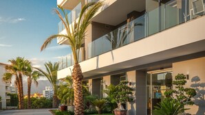 Een modern gebouw met een glazen balkon, palmbomen en een verzorgde tuin.
